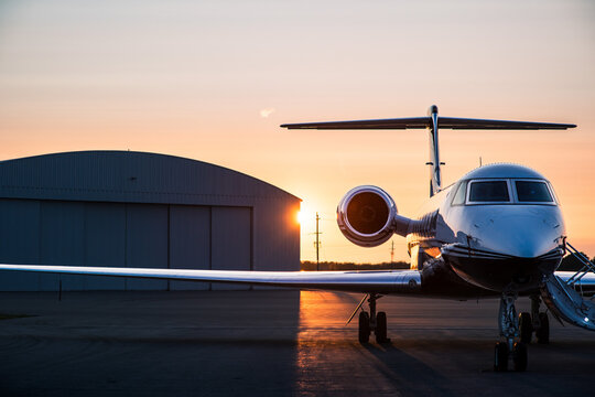 Private jet on tarmac at sunrise with stairway deployed and hangar in background