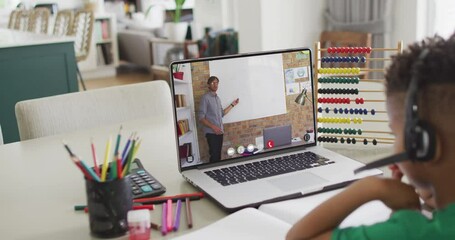 Diverse schoolboy having laptop video call with male teacher in slow motion - Powered by Adobe