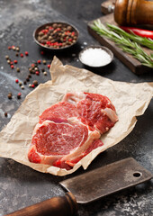 Rib eye raw fillet with meat hatchet,salt and pepper with rosemary on dark kitchen table.