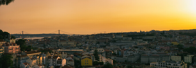 A breathtaking panoramic view of Lisbon at sunset, captured from the Miradouro da Nossa Senhora do Monte. The city’s vibrant colors and historic architecture are beautifully illuminated by the warm gl