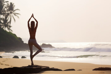 Fototapeta na wymiar A woman practices yoga on a tropical beach. Back view.
