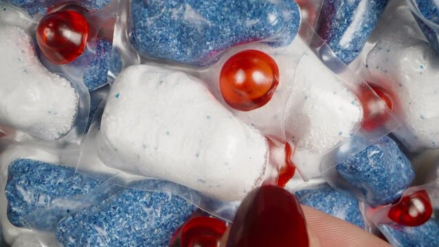 I take a single soluble packet with dishwasher powder, the camera lifts up while the capsule spins, close-up.
