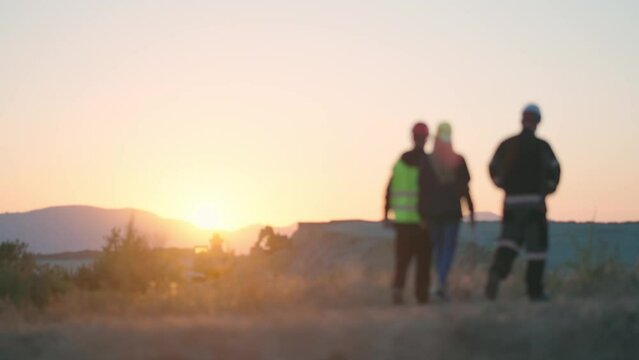 Engineers wearing a protective equipment walk at construction site at sunset, slow motion