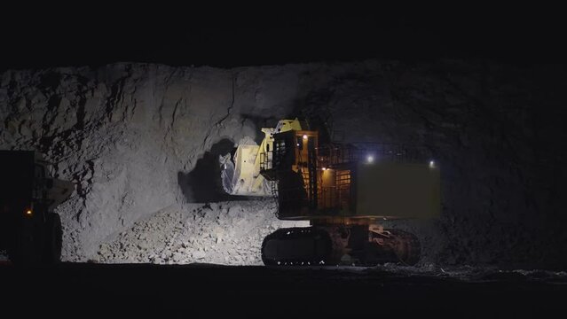 Large escavator loading ore rock in dumper truck at night, slow motion