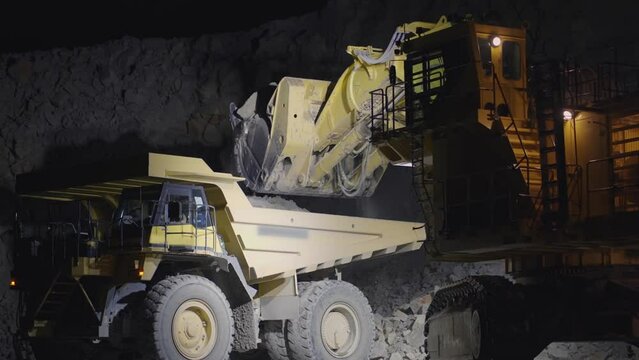 Excavator loading crushed stone into a dump truck in a crushed gold mine stone quarry, slow motion