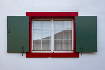 Picturesque window with open shutters on white wall of house, Swiss heritage, downtown. Discreet, laconic style of Switzerland in dark red and green colors
