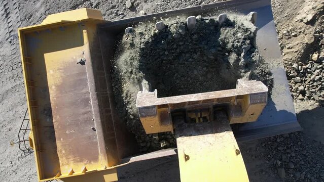 Large bucket excavator loads ore into a large dump truck in open mine gold digging pit, slow motion aerial shot