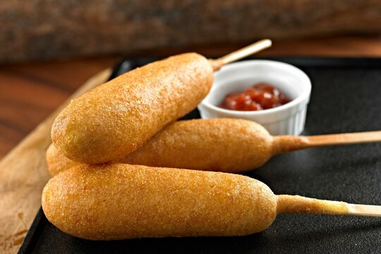 Classic Fair Delight: Close-Up of a Corn Dog Served with Ketchup on a Wooden Background, Tempting Your Taste Buds in 4K Resolution