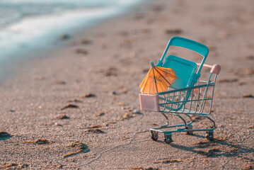 Shopping basket with chair and umbrella. The concept of summer sale and shopping for the beach season for relaxation.