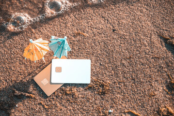 Top View Of Wet Sand With Bank Cards And Cocktail Umbrellas. Concept Of Limitless Possibilities. Concept Of Reliability Of Bank Cards With Completed Transactions and Expenses Tracking On Beach Holiday