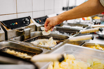 Chef cooking delicious potato chips in hot oil on kitchen