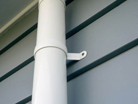 White plastic downpipe with bracket screwed to the wall