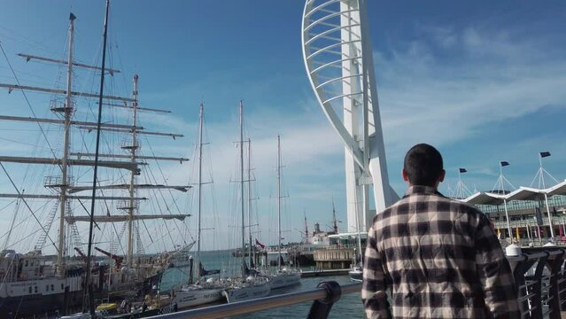 Tourist man walk on pier of Portsmouth harbor entrance with surrounding buildings, Spinnaker tower and ferries, slow motion