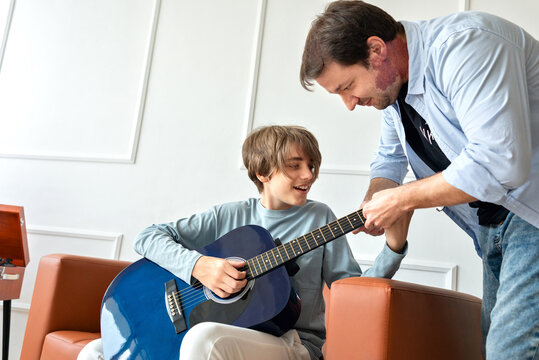 Single parent family relations, fathers support and care. Father teaching teenager son to playing acoustic guitar indoor.