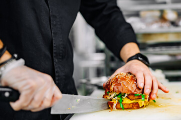 burger with beef, tomato, cheese, and lettuce chef cutting on kitchen