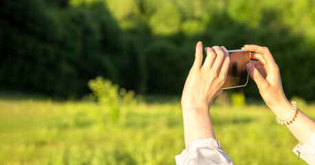 Hands holding mobile phone, taking photo outdoors. Banner background