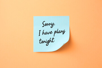 Light blue sticky note with phrase Sorry, I Have Plans Tonight on pale orange background