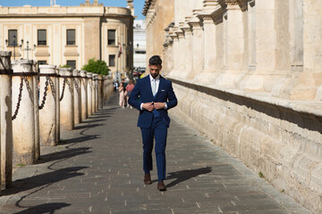 Handsome young man with beard and dressed in blue suit and tie, walks by the cathedral of seville in spain. The man is an executive who is in the city on a business trip.