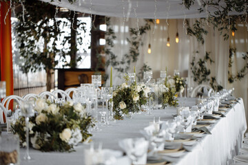 Wedding decor, table setting with white dishes, glass glasses and flowers, against the background of lanterns.