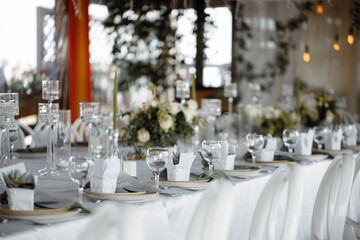 Wedding decor, table setting with white dishes, glass glasses and flowers, against the background of lanterns.