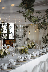Wedding decor, table setting with white dishes, glass glasses and flowers, against the background of lanterns.