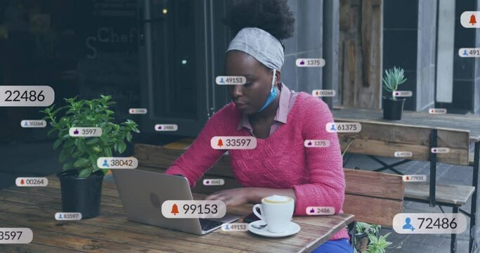 Animation of social media icons over african american woman using laptop at a cafe