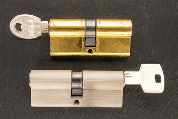 Two door lock cylinders and keys on slate stone, macro, top view.