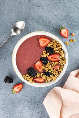 Smoothie bowl with strawberries, blackberries and granola on a blue background. Healthy breakfast. Top view.