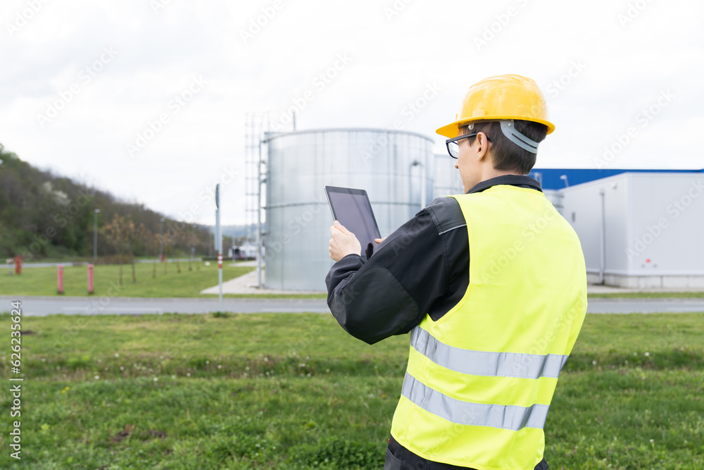 Poster engineer with digital tablet on a background of gas tanks