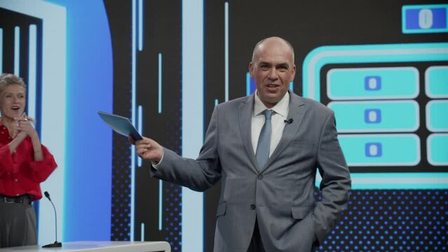 Funny charismatic host talking to the camera during recording of a fictional morning family game show