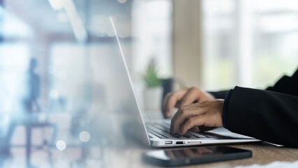 Executive's Workspace: Businessman in Black Suit Typing on Notebook Computer at Office Desk