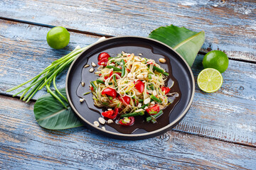 Traditional Thai green papaya som tam salad with green papaya slices, cherry tomatoes and beans in sweet sour fish sauce served as close-up on a Nordic design plate
