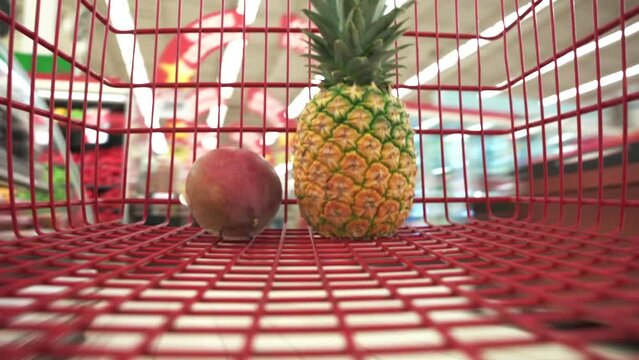 Timelapse close up view the buyer puts fresh fruits and berrys in the red shopping cart in a grocery supermarket. Healthy proper nutrition for the whole family