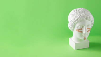 Beige tapes for the face on the bust on a green background. Non-surgical facelift, rejuvenation. Copy space