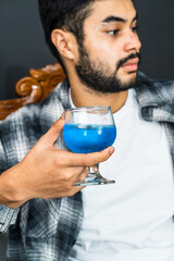 Artfully arranged, the image captures a man elegantly showcasing a blue colored drink, perfect for adding vibrancy to your visual storytelling