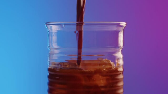 Bartender pours coffee frop pot into a narrow fluted glass on fashionable modern bar counter with neon lighting. Making ice coffee cocktail on a beautiful colored background at party. Close up macro