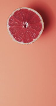 Vertical video of halved red grapefruit with copy space over red background