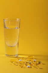 Diet, nutrition, healthy eating concept. Assorted Oil filled yellow softgels capsules and pills of food supplements and glass of water for pouring on yellow background