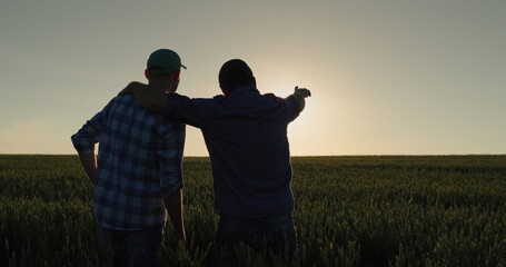 A man and his son watch the sunrise over a wheat field together. Farmers in the field and family...