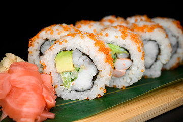 Set of California rolls with avocado, cucumber, shrimp covered orange tobiko caviar with red, white ginger and wasabi nearby