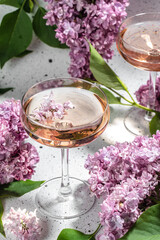 Rose wine in glass with blooming lilac on a light background
