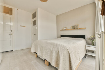 a bedroom with white walls and wood flooring the room has a large bed, wooden shelves on either side