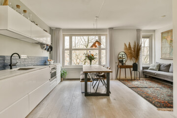 a kitchen and living room in an apartment with white cabinets, wood flooring and large windows looking out onto the street