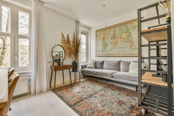 a living room with a map hanging on the wall and a grey couch in the room is surrounded by white curtains