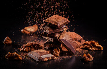 A pile of dark broken chocolate sprinkled with cocoa powder and walnuts on a dark background