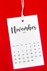 The November 2023 calendar page for 2023 year hanged on white rope on Red background.