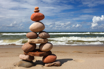 Stone zen pyramid made of colorful pebbles on the beach against a stormy sea.