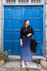 Young happy Caucasian woman  posing and smiling in front of a blue door. Cheerful people outdoor.