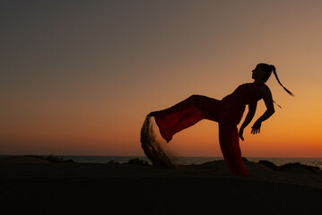 Silhouette of a woman dancing at a sandy beach at sunset. Caucasian woman posing outdoors at the coast.