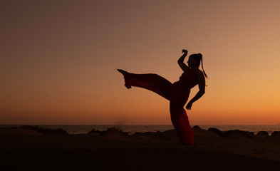 Silhouette of a woman dancing at a sandy beach at sunset. Caucasian woman posing outdoors at the coast.